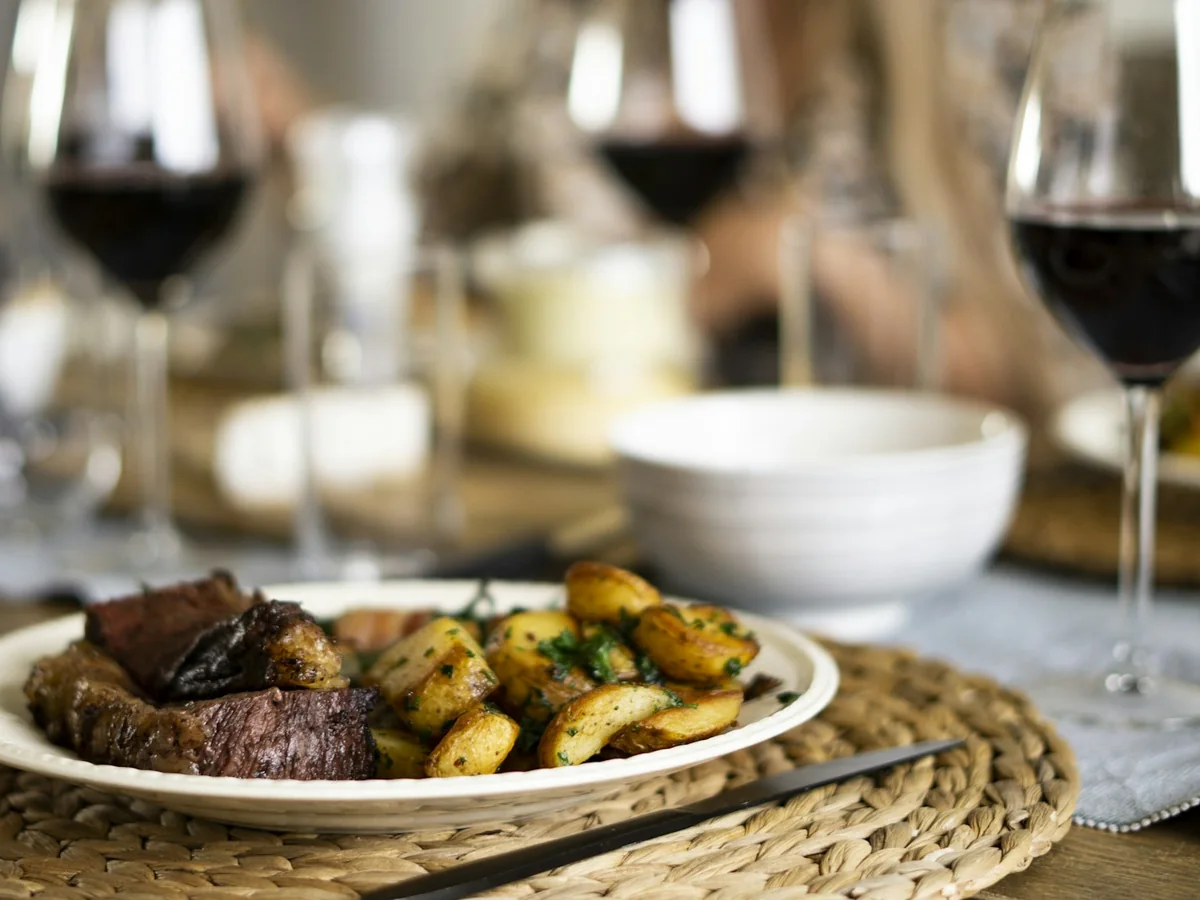 A plated steak dinner with roasted potatoes and glasses of red wine on a table (representative photograph, not La Ventana's own dining room)